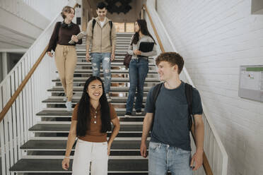 Happy multiracial students talking while moving down on steps in university - MASF39069