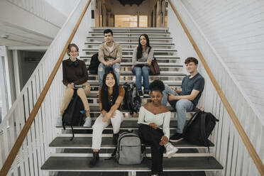 Porträt eines glücklichen Studenten und einer Studentin, die auf einer Treppe in einer Universität sitzen - MASF39071