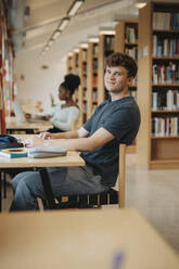 Porträt eines lächelnden Studenten, der am Tisch sitzt und in der Bibliothek studiert - MASF39088