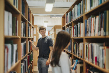 Happy students searching books on bookshelf in library at university - MASF39095