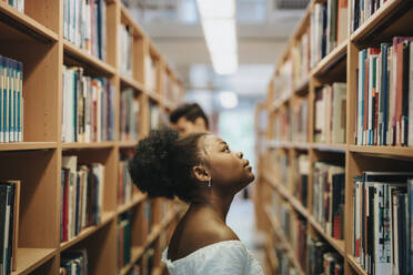 Side view of student searching books on bookshelf in library at university - MASF39099