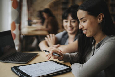 Smiling female students discussing over book at library - MASF39103