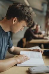 Male student reading book in library at university - MASF39107