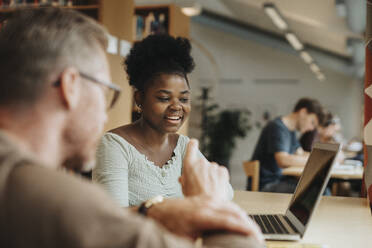 Smiling student discussing with professor over laptop in library at university - MASF39112