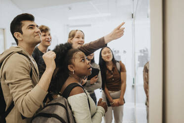 Multiracial male and female students checking result on bulletin board in university - MASF39118