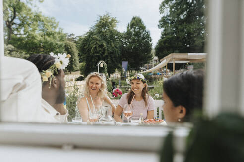 Glückliche junge Frauen, die sich mit Freunden auf einer Dinnerparty vergnügen, gesehen durch ein Fenster - MASF39130