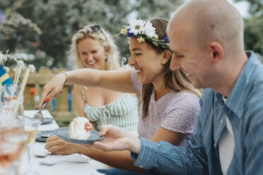 Glückliche junge Frau, die eine Tiara trägt, während sie einem männlichen Freund während einer Dinnerparty im Café Kuchen serviert - MASF39144