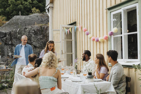 Lächelnde Frau serviert Essen an männliche und weibliche Freunde während einer Dinnerparty im Café - MASF39154