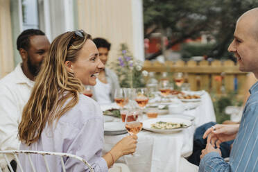 Glückliche junge Frau hält ein Weinglas in der Hand und lacht mit einem männlichen Freund während einer Dinnerparty im Café - MASF39161