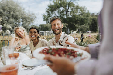 Glückliche männliche und weibliche Freunde lachen, während sie bei einer Dinnerparty am Tisch sitzen - MASF39165