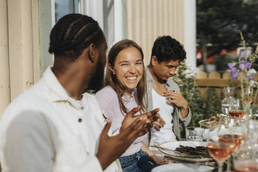 Glückliche junge Frau, die einen männlichen Freund ansieht, der sich während einer Dinnerparty im Café unterhält - MASF39166