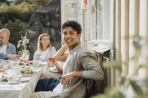 Seitenansicht Porträt eines lächelnden jungen Mannes sitzt auf einem Stuhl mit Freunden während des Abendessens Partei im Café - MASF39173