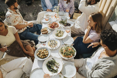 High angle view of male and female friends enjoying food during dinner party at cafe - MASF39180