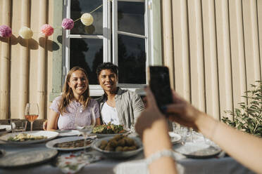 Hand einer Frau, die ein Bild von männlichen und weiblichen Freunden während einer Dinnerparty im Café anklickt - MASF39181