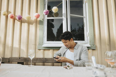 Young man using smart phone while sitting at table during dinner party - MASF39184