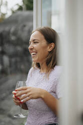 Happy woman laughing while holding wineglass during dinner party at cafe - MASF39223