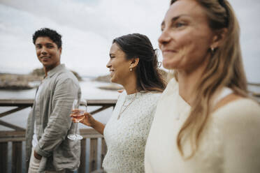 Glückliche Frau mit Wein in der Hand beim Spaziergang mit Freunden auf einer Brücke - MASF39228