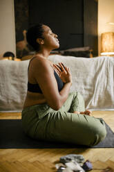 Side view of young woman meditating in bedroom at home - MASF39270