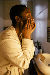 Young woman applying moisturizer on face at home - MASF39277