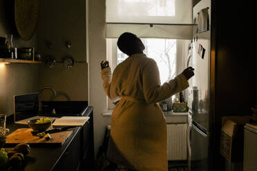 Carefree young woman wearing bathrobe dancing in kitchen at home - MASF39280