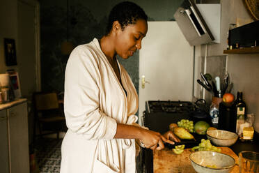 Side view of young woman cutting kiwi at kitchen counter - MASF39285