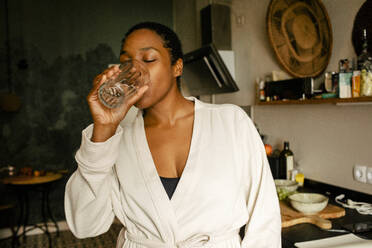 Young woman drinking water while standing in kitchen at home - MASF39287