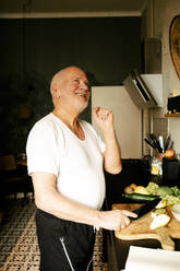 Happy senior man chopping fruits in kitchen at home - MASF39302