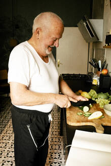 Glücklicher älterer Mann hackt Gemüse in der Küche zu Hause - MASF39303