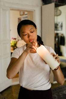 Junge Frau steht mit einer brennenden Kerze zu Hause - MASF39307