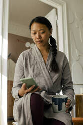 Young woman using smart phone while having coffee at home - MASF39325