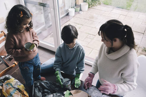 Hochformatige Ansicht einer Mutter mit Kindern, die zu Hause Abfall sammeln - MASF39354