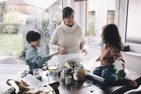 Happy woman separating waste with son and daughter at home - MASF39357