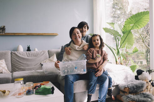 Portrait of cheerful family with plastic waste sitting in living room at home - MASF39360