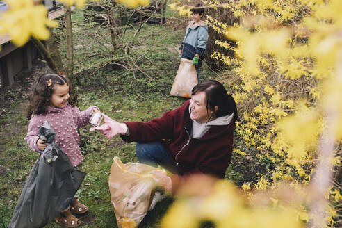 Glückliche Mutter sammelt mit Tochter und Sohn im Hinterhof Müll - MASF39365
