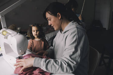 Tochter sieht Mutter beim Nähen von Kleidung zu Hause zu - MASF39375