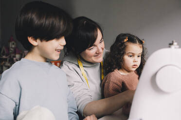 Smiling mother with son and daughter looking at sewing machine - MASF39376