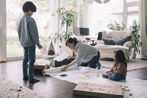 Mutter mit Sohn und Tochter, die im Wohnzimmer zu Hause auf einem Stoff zeichnen - MASF39379