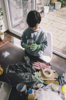 High angle view of boy holding glass container at home - MASF39385