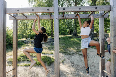 Girls practicing monkey bars while playing during summer camp - MASF39391