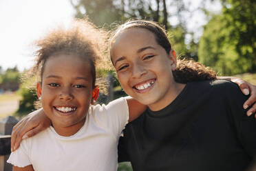 Portrait of happy female friends sitting with arms around at summer camp - MASF39400