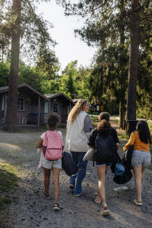 Rear view of camp counselor walking with girls on footpath at summer camp - MASF39433