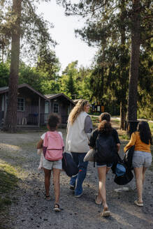 Rückansicht einer Betreuerin, die mit Mädchen auf einem Fußweg im Sommerlager spazieren geht - MASF39433