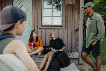 Mädchen lachen, während sie sich mit einem Betreuer unterhalten, der bei einer Hütte im Ferienlager steht - MASF39441