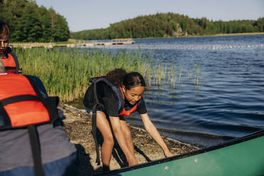 Mädchen trägt Schwimmweste und hält Kajak in der Nähe des Sees im Sommerlager - MASF39452