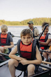 Porträt eines Jungen, der eine Schwimmweste trägt, während er im Kajak im Sommerlager sitzt - MASF39458