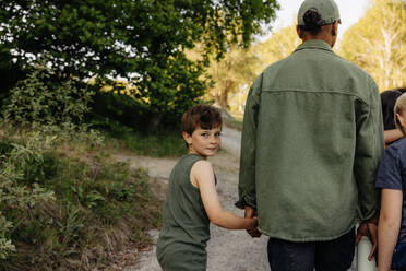 Porträt eines Jungen, der die Hand eines Betreuers hält, während er auf dem Fußweg im Ferienlager geht - MASF39467
