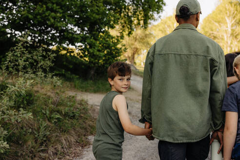 Porträt eines Jungen, der die Hand eines Betreuers hält, während er auf dem Fußweg im Ferienlager geht - MASF39467