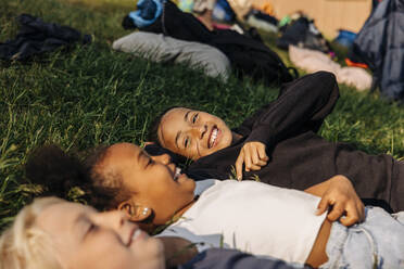 Happy girl enjoying with friends while lying down on grass at summer camp - MASF39472