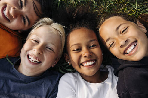 Portrait of cheerful kids lying together on grass at summer camp - MASF39476