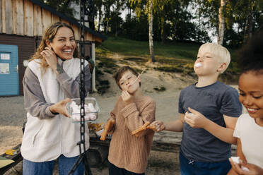 Children having snacks with counselor holding container at summer camp - MASF39478